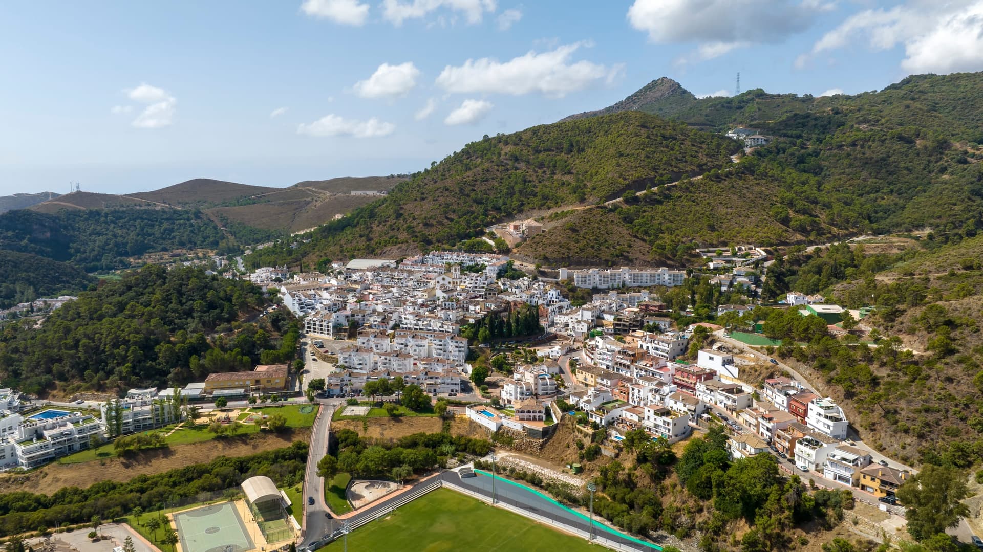 Aerial view of the white village of Benahavís among green, wooded hills