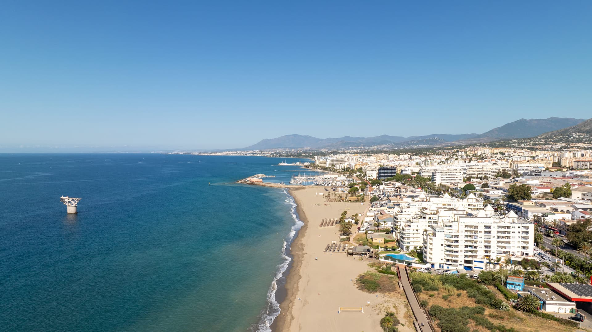 Aerial view of the Marbella seafront: the beach, the marina and the town, with the mountains behind